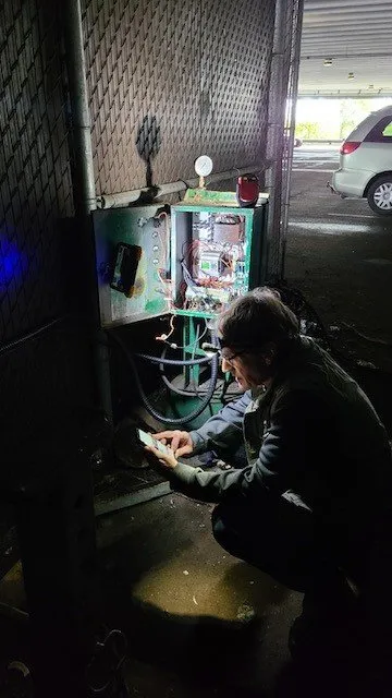 WasteMind technician diagnosing a compactor control panel in a building parking garage